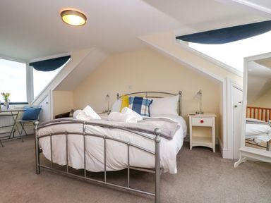 A bedroom with a metal bed frame small bedside tables a floor mirror and a window with a small table and chair at Breakers Point in St Ives