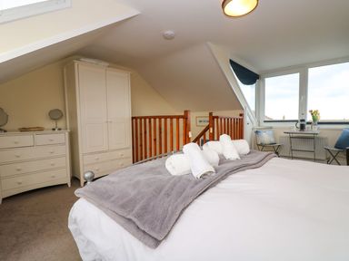 A bedroom with a bed with rolled towels on a gray blanket a wardrobe and chest of drawers and a small table with two chairs by the window at Breakers Point in St Ives