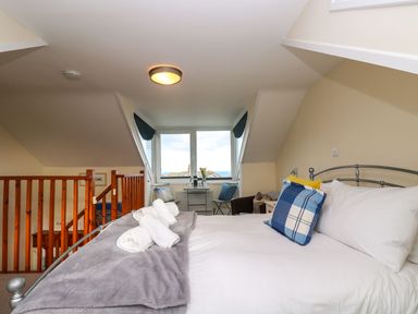 A bedroom with a bed and pillows near a window and wooden staircase railing at Breakers Point in St Ives