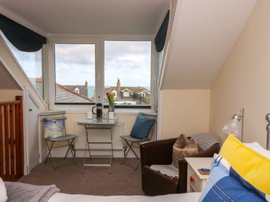 A small seating area with two metal chairs and a table by a window overlooking rooftops and the sea at Breakers Point in St Ives