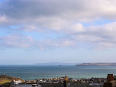 A coastal town with rooftops in the foreground and a sea view with an island and cliffs in the background at Breakers Point in St Ives