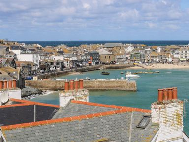 A coastal town with stone buildings rooftops harbor wall and boats in the water at Breakers Point in St Ives