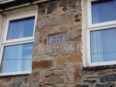 A stone wall with windows and a plaque stating GAG 1859 at Rhianfa Newborough