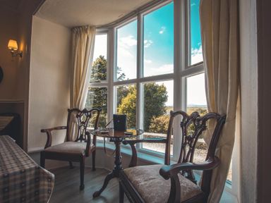 A sitting room with two chairs and a table by a large window at Noddfa Country House Harlech