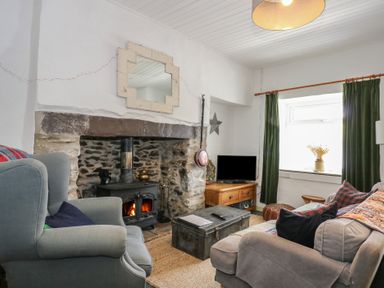 A living room with a wood stove fireplace armchairs a sofa a coffee table and a television at Cobweb Cottage in Waunfawr