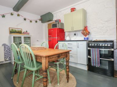 A kitchen with a wooden dining table and green chairs a red refrigerator a black oven and white cabinets at Cobweb Cottage in Waunfawr