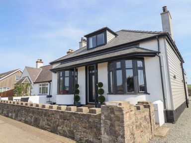 A detached house with a stone wall and a front door flanked by two topiary plants at Bronallt in Cemaes Bay