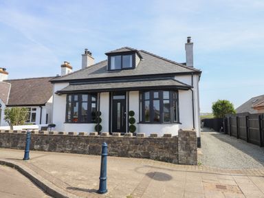 A detached house with black framed windows and door a stone wall and a driveway at Bronallt in Cemaes Bay