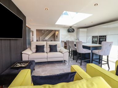A living room and kitchen area with a sofa two yellow chairs a dining table with grey chairs and a skylight at Bronallt in Cemaes Bay