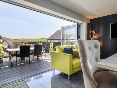 A living room with yellow chairs and a table with chairs outside at Bronallt in Cemaes Bay