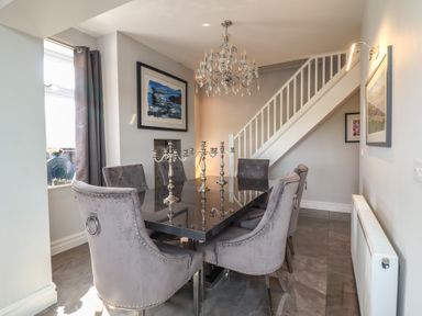 A dining room with six grey chairs around a black table and a chandelier overhead at Bronallt in Cemaes Bay