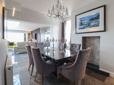A dining room with a black table and grey upholstered chairs under a chandelier at Bronallt in Cemaes Bay