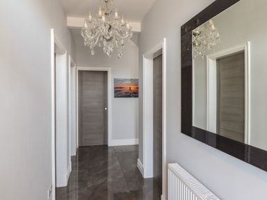 A hallway with closed gray doors a chandelier a large mirror and a radiator at Bronallt in Cemaes Bay