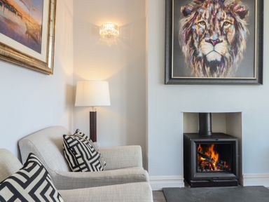 A living room with two armchairs a lit fireplace and lion painting above at Bronallt in Cemaes Bay