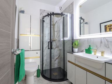 A bathroom with a glass shower enclosure toilet sink with gold fixtures and green accessories at Bronallt in Cemaes Bay