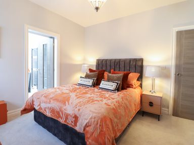 A bedroom with a bed with orange bedding and pillows two bedside tables with lamps and an open door leading to a bathroom at Bronallt in Cemaes Bay