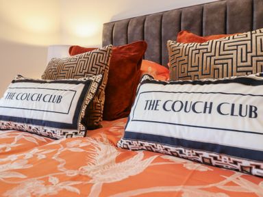 A bed with patterned pillows and cushions with the text The Couch Club at Bronallt in Cemaes Bay