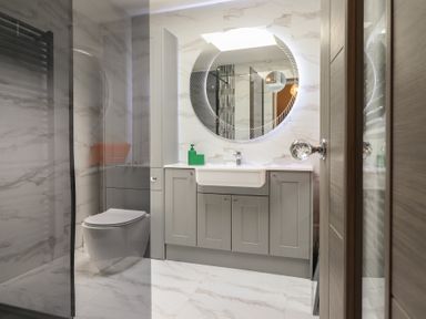 A bathroom with a toilet, sink with cabinets, a round mirror, and a shower area at Bronallt in Cemaes Bay