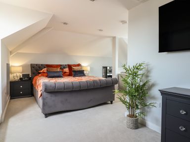 A bedroom with a large bed with pillows lamps on bedside tables a plant and a mounted TV at Bronallt in Cemaes Bay