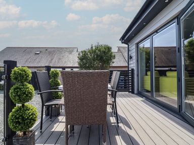 An outdoor deck with wicker chairs and a table next to sliding glass doors and potted plants at Bronallt in Cemaes Bay