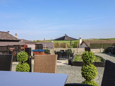 An outdoor patio area with woven chairs a table umbrella and green plants at Bronallt in Cemaes Bay