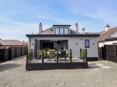 A house with an open patio door leading to an outdoor seating area with a table and chairs at Bronallt in Cemaes Bay