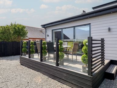 An outdoor patio with glass and black wood railing with chairs and a table at Bronallt in Cemaes Bay