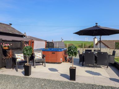 An outdoor patio area with chairs and cushions a hot tub dining table with chairs and an umbrella at Bronallt in Cemaes Bay