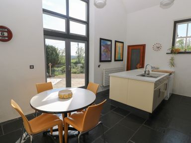 A kitchen with a round table and four chairs near glass doors and an island with a sink at Zoar Chapel in Carew