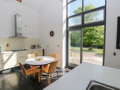 A kitchen with a round table and four orange chairs near large windows showing trees outside at Zoar Chapel in Carew
