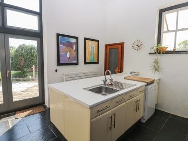 A kitchen with an island sink cabinet dishwasher wall clock and framed pictures at Zoar Chapel in Carew