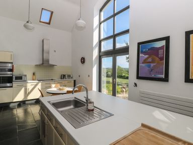 A kitchen with a sink on an island and a round dining table near large windows at Zoar Chapel in Carew