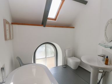 A bathroom with a bathtub toilet sink mirror arched window and skylight at Zoar Chapel in Carew