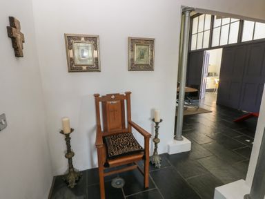 A wooden chair with a patterned cushion between two candlesticks and religious artwork on the wall at Zoar Chapel in Carew