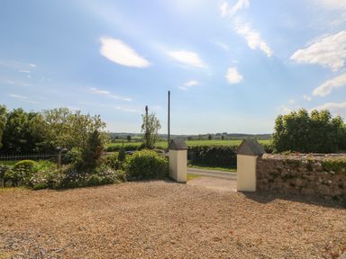 A gravel driveway with garden beds and an open gate leading to a road and fields at Zoar Chapel in Carew