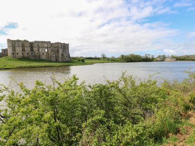 Ruins of a stone castle beside a river with green bushes in the foreground and houses in the background at Zoar Chapel in Carew