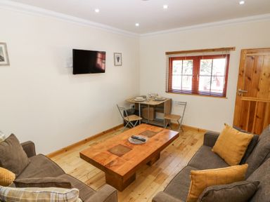 A living room with two sofas a wooden coffee table a wall-mounted TV and a small dining table with two chairs at Smiddy Bothy Edzell