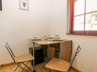 A small dining area with a square table set for two near a window with blinds at Smiddy Bothy Edzell