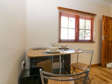 A small dining table set with two place settings and two chairs by a window with wooden blinds at Smiddy Bothy in Edzell