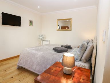 A bedroom with a bed, bedside table with lamp, wall-mounted TV, fan, and a mirror at Smiddy Bothy in Edzell