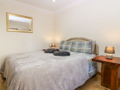 A bedroom with a double bed two side tables with lamps a mirror on the wall and folded towels on the bed at Smiddy Bothy in Edzell