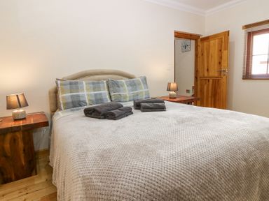 A bedroom with a double bed with folded towels on top two wooden bedside tables with lamps and a wooden door at Smiddy Bothy in Edzell