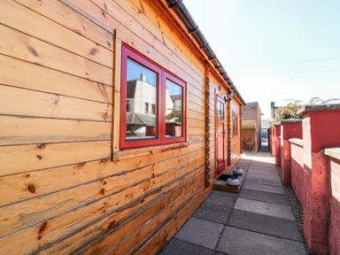 A walkway beside a wooden building with red windows and door at Smiddy Bothy in Edzell