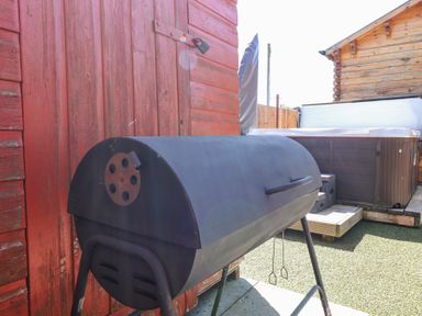 A charcoal barbecue grill next to a red wooden shed and a hot tub on a patio at Smiddy Bothy in Edzell