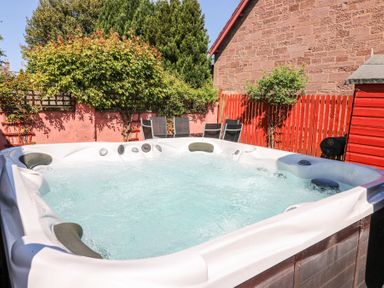 An outdoor hot tub with bubbling water near a red fence and garden chairs at Smiddy Bothy in Edzell