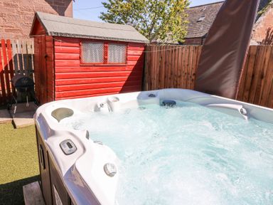 An outdoor hot tub with bubbles next to a red wooden shed and a wooden fence at Smiddy Bothy in Edzell