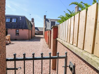 A gravel driveway leading to houses with sloped roofs and fences on the side at Smiddy Bothy in Edzell