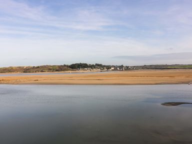 A view of a river with sandy banks and a village with houses and trees in the background at Lodge 9- Lamorna in Tregolds near St Merryn