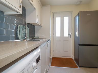 A kitchen with a washing machine under the counter a stainless steel sink a drying rack a refrigerator and a white door with windows at Lodge 18 in St Merryn