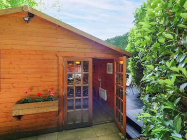A wooden cabin with a door and flowers in a planter at Stumps Cross Lodge Upper Coscombe near Winchcombe